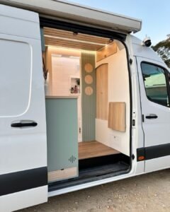 Área de entrada do motorhome Sprinter 416 Extra Longa, com mesa retrátil e banco embutido, em design moderno.
