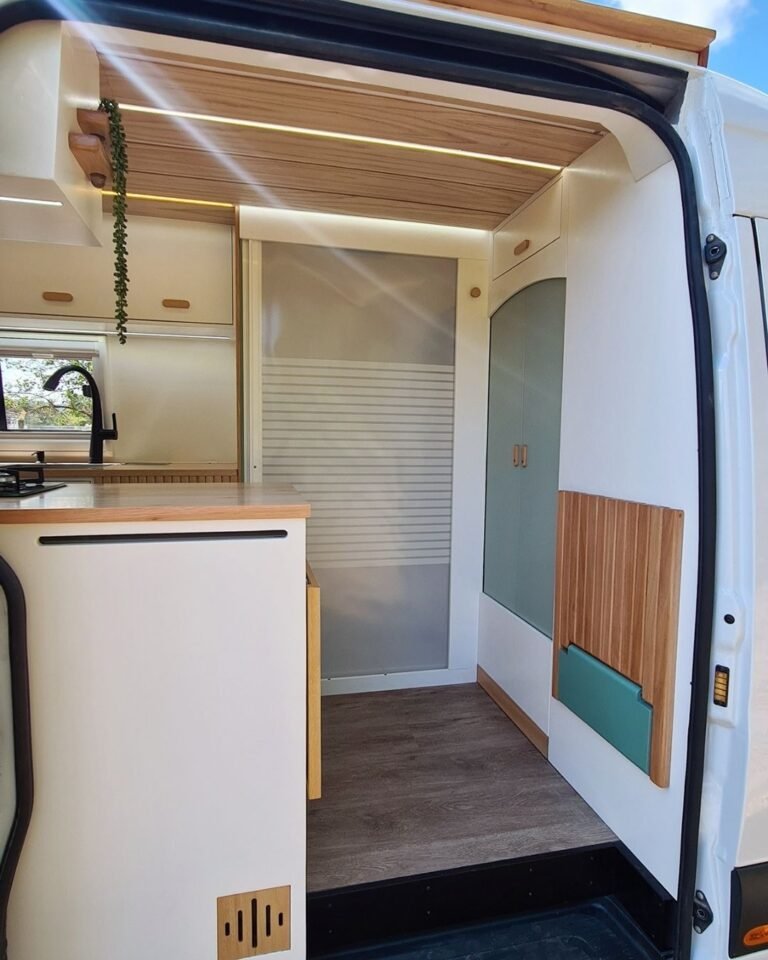 Área de entrada da Sprinter 416 Extra Longa, com mesa retrátil e banco embutido, em tons claros e design moderno